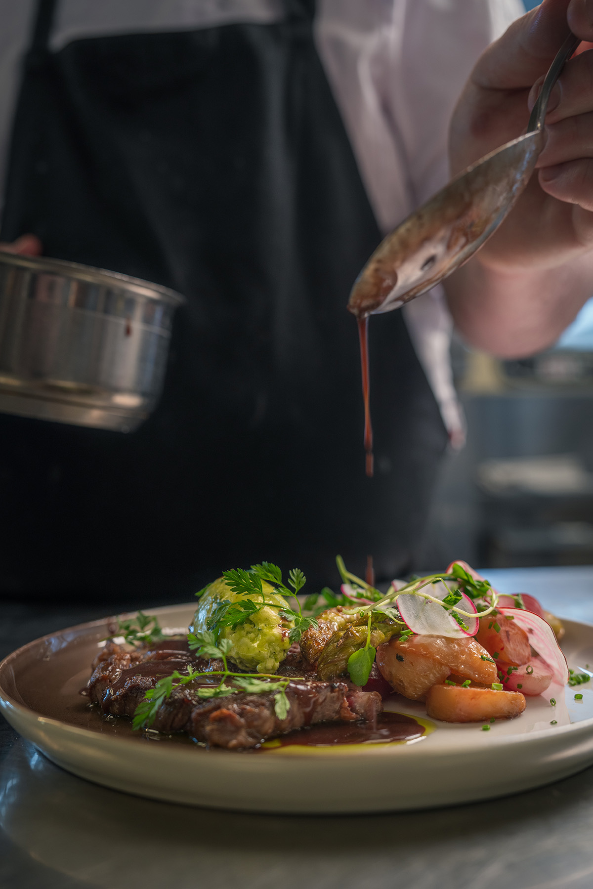 En kock häller på sås på en tallrik med kött och rotfrukter