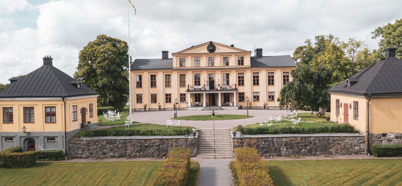 Herrgårdsbyggnaden omgiven av grönskande miljöer