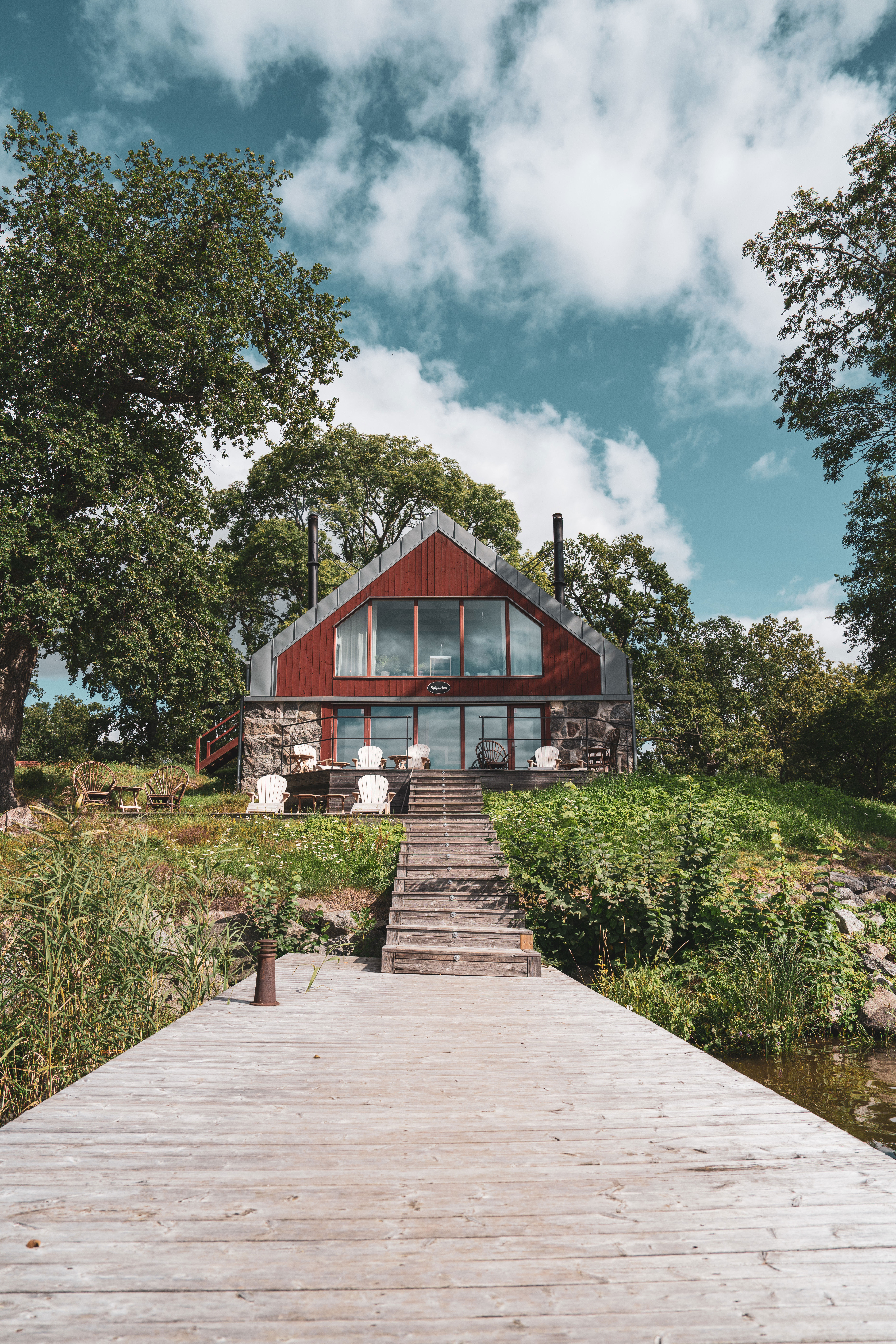 Grönska omringar en stor röd bastu med tillhörande brygga 