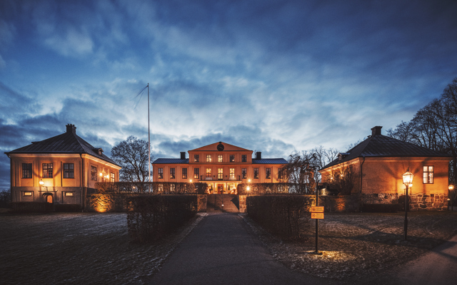 Herrgårdens fasad upplyst av lampor en höstkväll